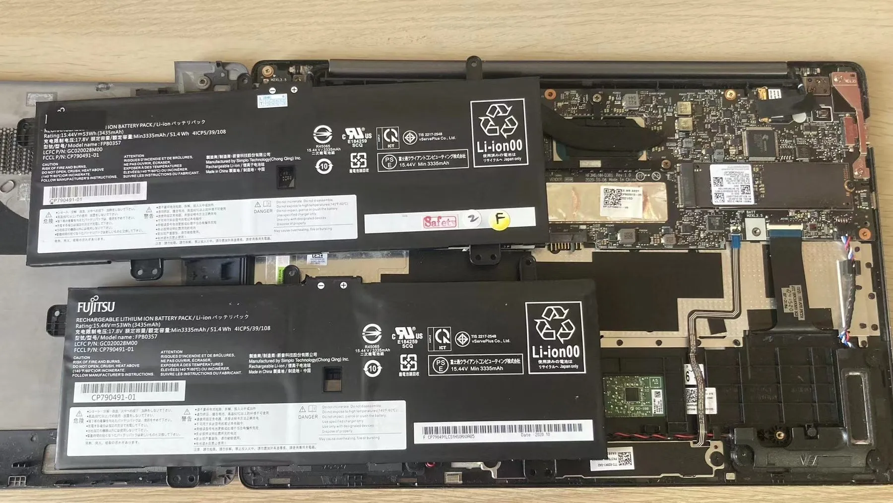 A laptop opened on a workbench with the battery and mainboard exposed during a repair