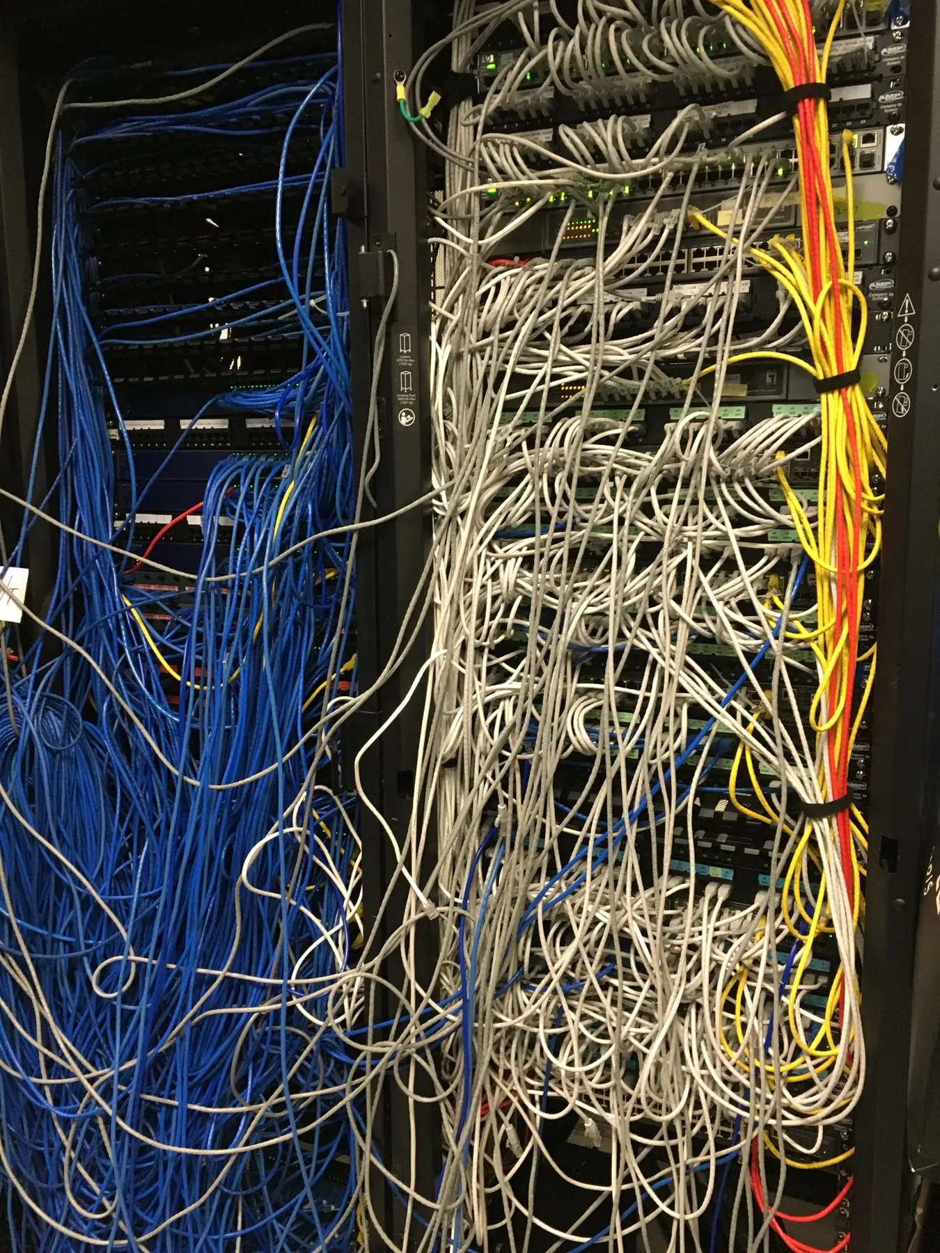 A server rack packed with unmanaged blue and white patch cables before remediation